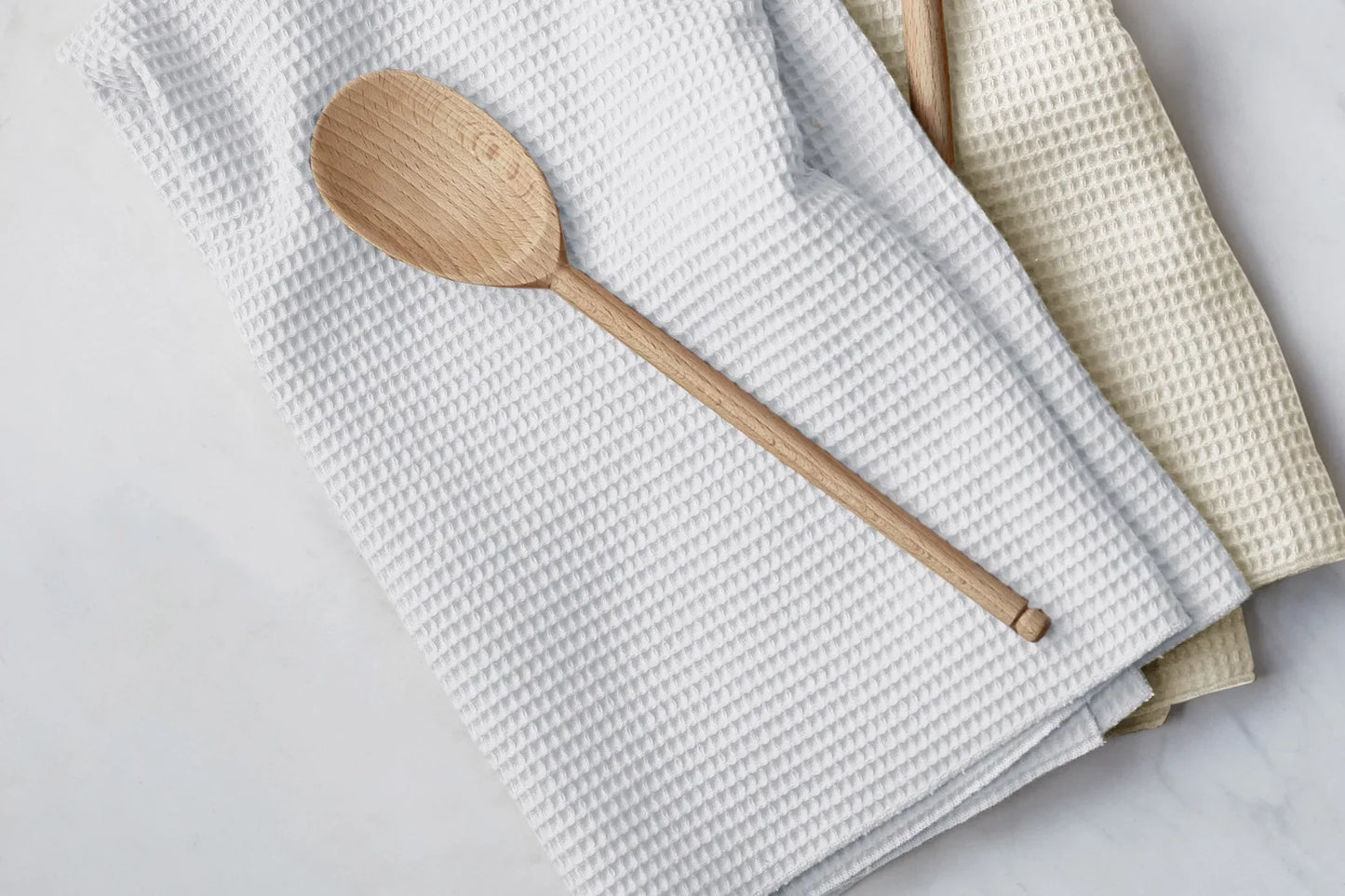 Wooden spoon on waffle textured white and beige kitchen towels on marble surface
