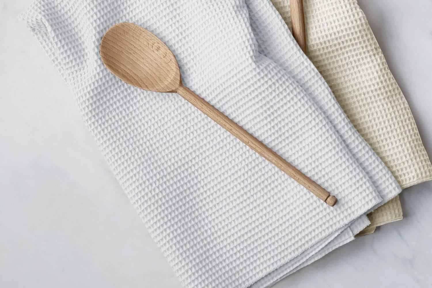 Wooden spoon resting on white and beige waffle weave kitchen towels on marble surface