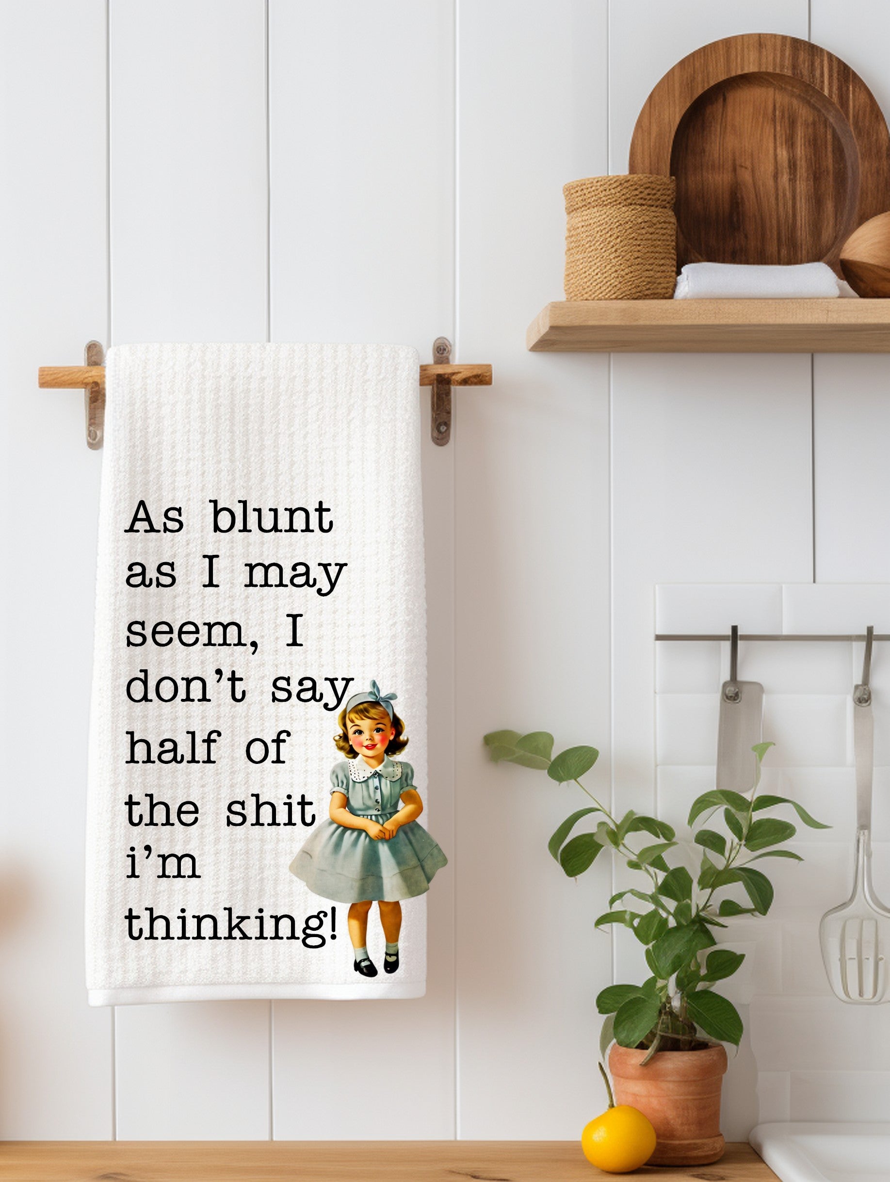 White kitchen towel with humorous blunt quote and vintage girl illustration hanging on wooden rack