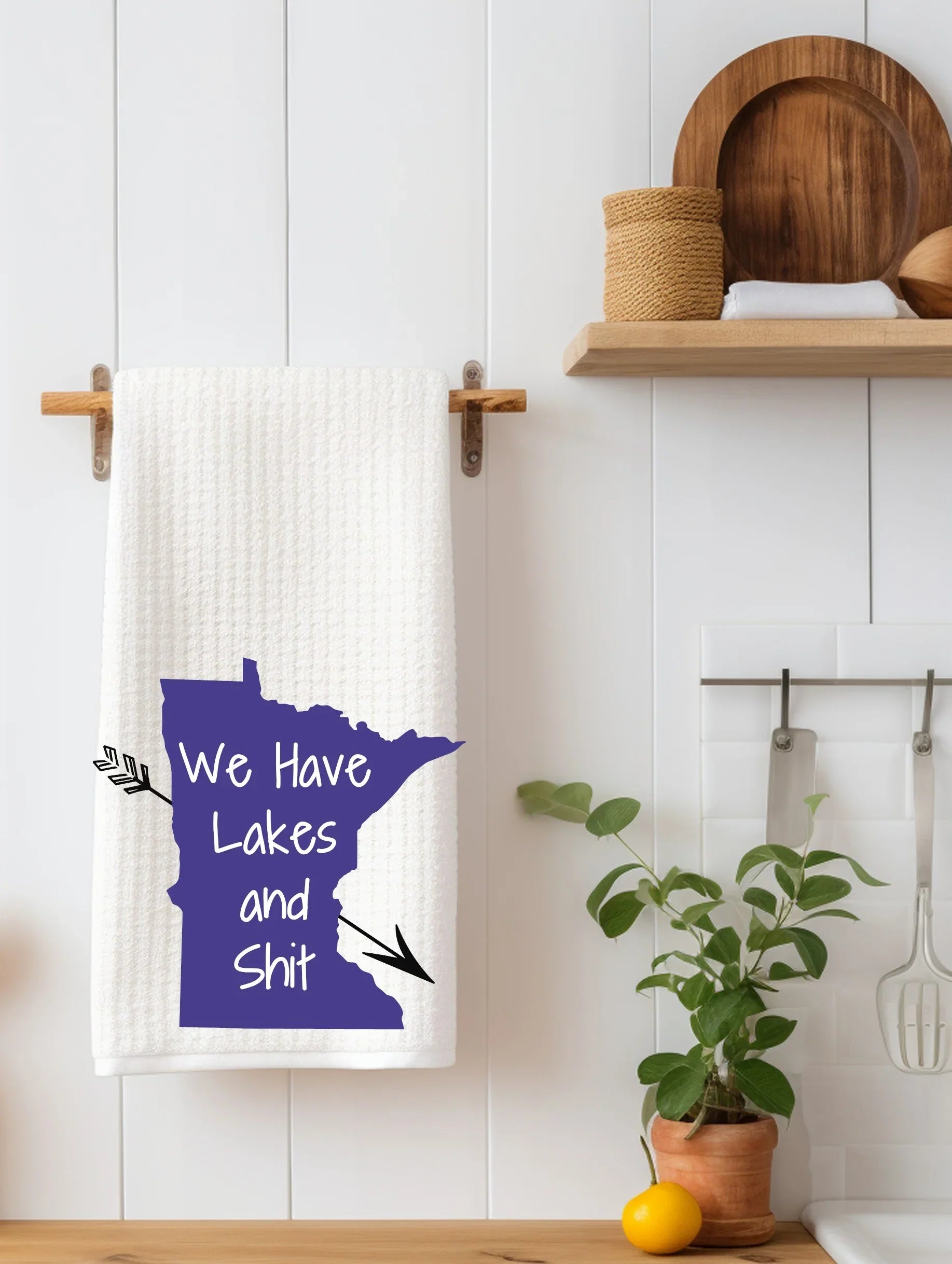 White towel hanging on wooden rack with purple Minnesota state shape and text We Have Lakes and Shit